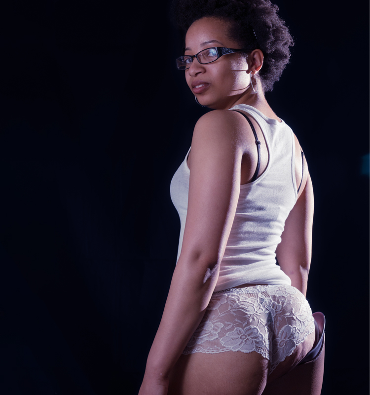 Keri Gray in a white tank top and white lace panties. Her back and booty is the focus of the image with a clear view of her right prosthetic leg.