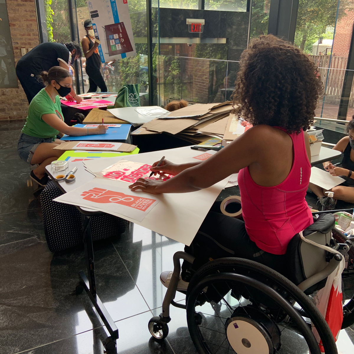 A group of folks making posters for the protest. One person is in a wheelchair.