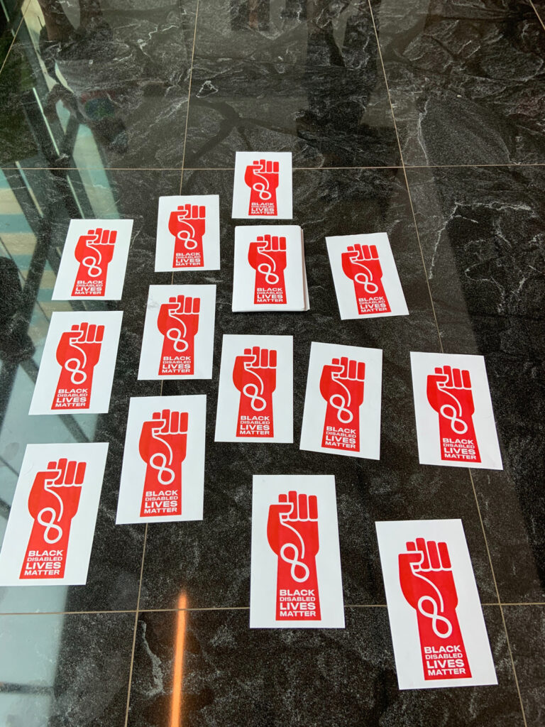 A group of posters across the floor. The posters are a red fist with the infinity sign that say Black Disabled Lives Matter. 